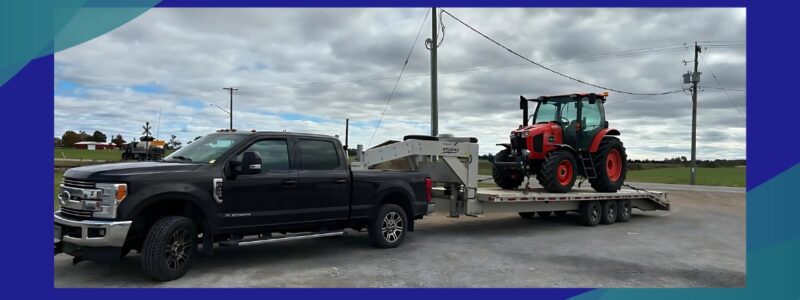 A black pickup truck towing a gooseneck trailer loaded with a red tractor, showcasing Millroad trailers' capability for heavy-duty hauling.