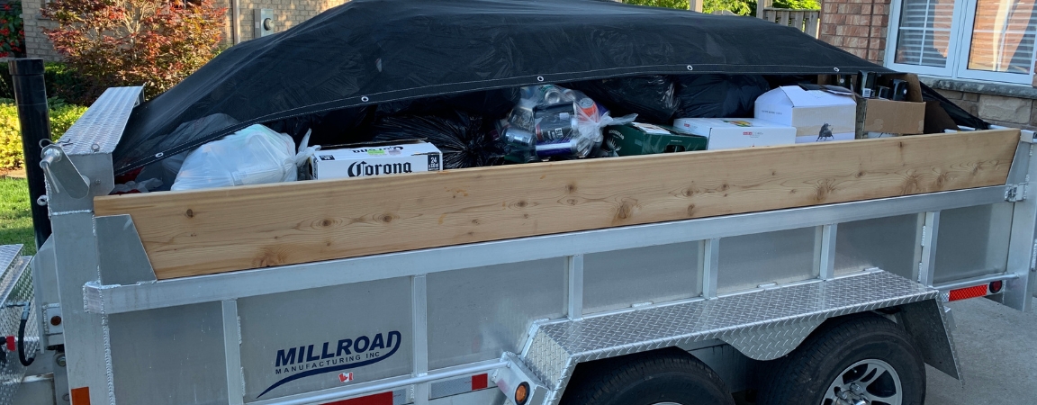 A Millroad aluminum dump trailer loaded with household items and waste, covered with a secured tarp, showcasing its utility for residential clean-up projects.